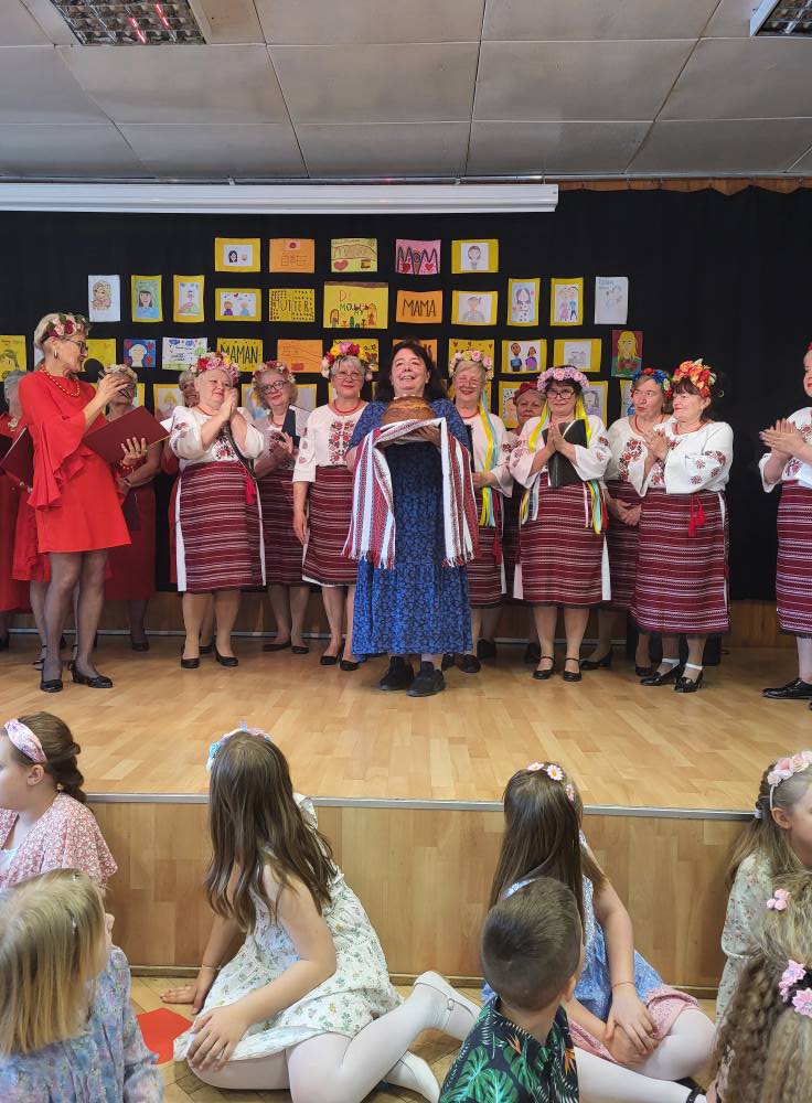 Zdjęcie przedstawia uczestniczki koncertu „Dla Ciebie, Mamo!” w klubie "Dąb": seniorki z Kapeli Dębowej i dzieci z Niepublicznej Szkoły Podstawowej LEGATO oraz panie z grupy "Ukraiński Wianuszek"