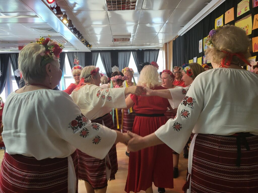 Zdjęcie przedstawia wspólny taniec na zakończenie koncertu „Dla Ciebie, Mamo!” w klubie "Dąb" w wykonaniu seniorek z Kapeli Dębowej, dzieci z Niepublicznej Szkoły Podstawowej LEGATO i pań z zespołu "Ukraiński Wianuszek" 