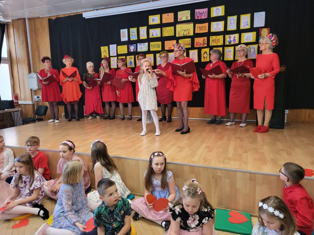 Zdjęcie przedstawia uczestniczki koncertu „Dla Ciebie, Mamo!” w klubie "Dąb": seniorki z Kapeli Dębowej i dzieci z Niepublicznej Szkoły Podstawowej LEGATO 