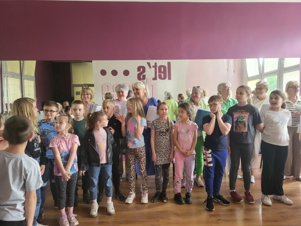 Zdjęcie przedstawia dzieci i seniorów biorących udział w próbie przed koncertem z okazji Dnia Matki w klubie "Dąb"