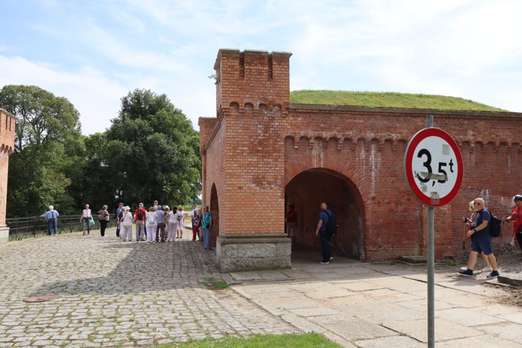 zdjęcie przedstawia uczestników wycieczki zwiedzających z lokalną przewodniczką Muzeum Twierdzy Kostrzyn
