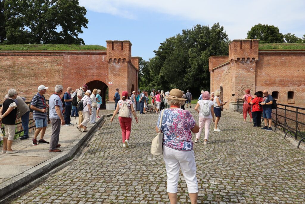 zdjęcie przedstawia uczestników wycieczki zwiedzających z lokalną przewodniczką Muzeum Twierdzy Kostrzyn