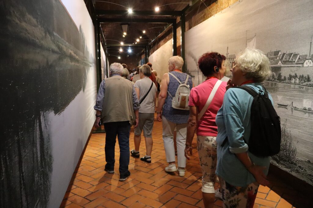zdjęcie przedstawia uczestników wycieczki zwiedzających z lokalną przewodniczką Muzeum Twierdzy Kostrzyn