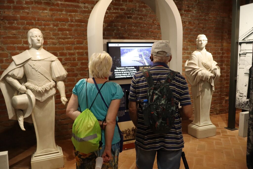 zdjęcie przedstawia uczestników wycieczki zwiedzających z lokalną przewodniczką Muzeum Twierdzy Kostrzyn