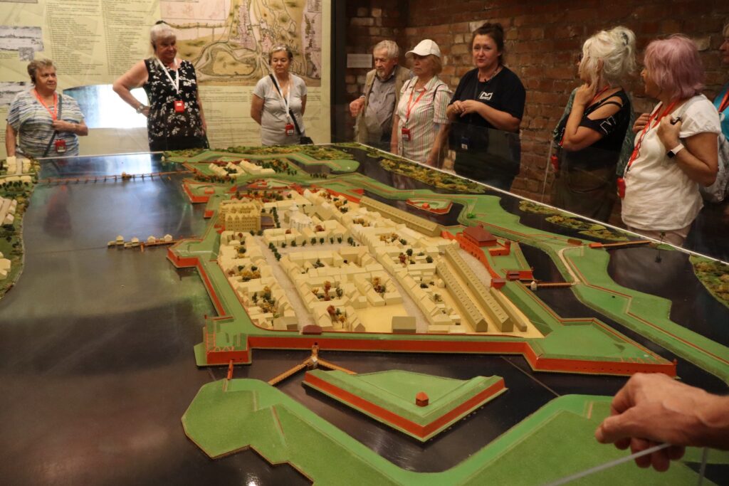 zdjęcie przedstawia uczestników wycieczki zwiedzających z lokalną przewodniczką Muzeum Twierdzy Kostrzyn