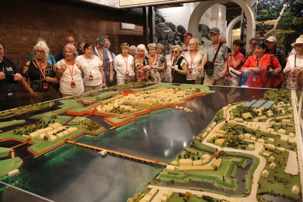 zdjęcie przedstawia uczestników wycieczki zwiedzających z lokalną przewodniczką Muzeum Twierdzy Kostrzyn